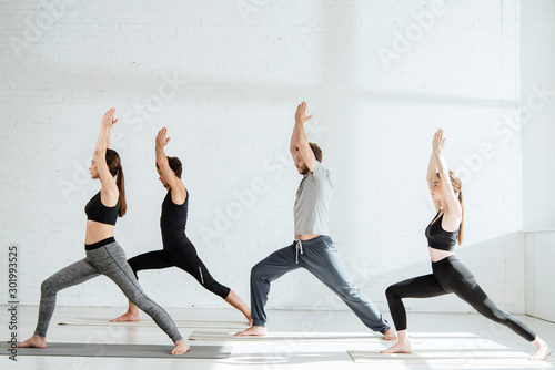 side view of young people in sportswear practicing yoga in warrior I pose