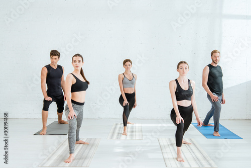 five young people practicing yoga in crescent lunge pose