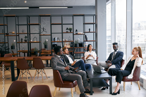 Internatonal group of business partners discuss future successful deal in modern office, wearing formal wear photo