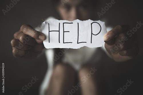 women sitting alone with depressed expression and showing a paper with a help text. Ideas to stop violence against women, sexual harassment and rape, human trafficking