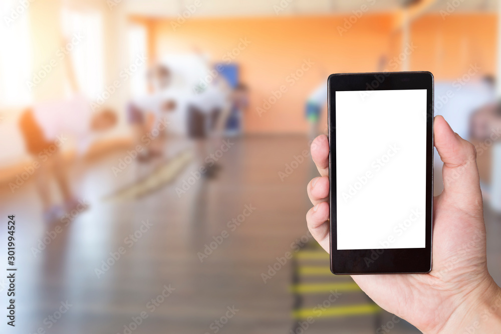 Hand with mobile phone in the background of people engaged in a fitness center. Gym and fitness phone app concept, copy space