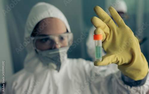 Female doctor with baceriological protective suit looking at an antidote vial for a dangerous virus photo