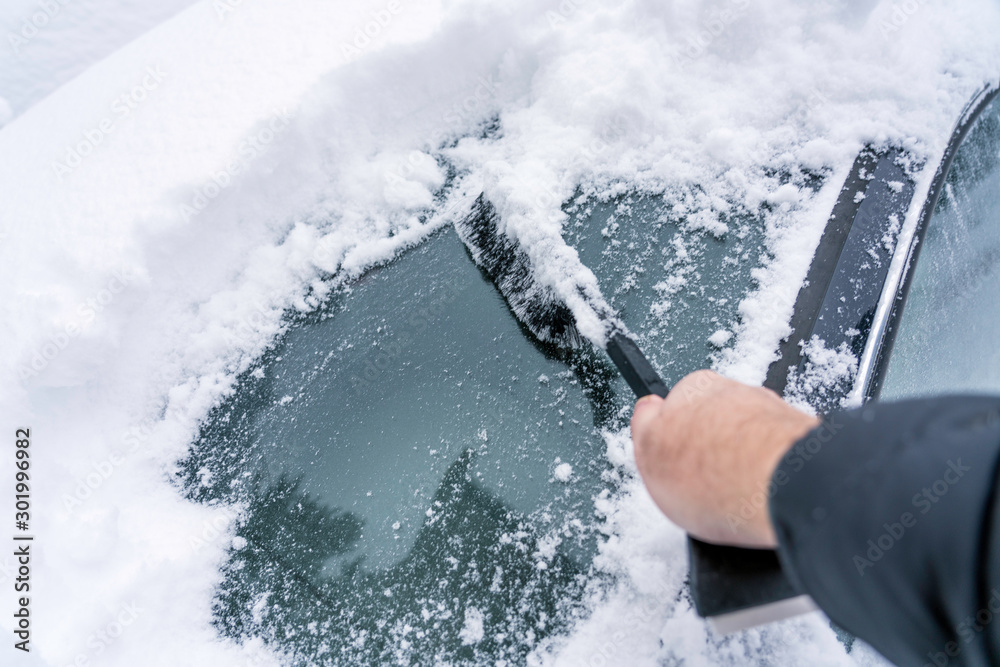 Hand are holding and brushing car window clean of snow. car covered in snow during heavy snow fall. Winter and seasonal concept. - obrazy, fototapety, plakaty 