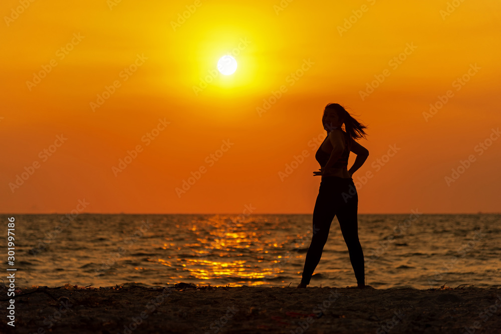Silhouette healthy woman lifestyle exercising vital meditate and practicing yoga on the rock in beach at sunset. Healthy Concept.
