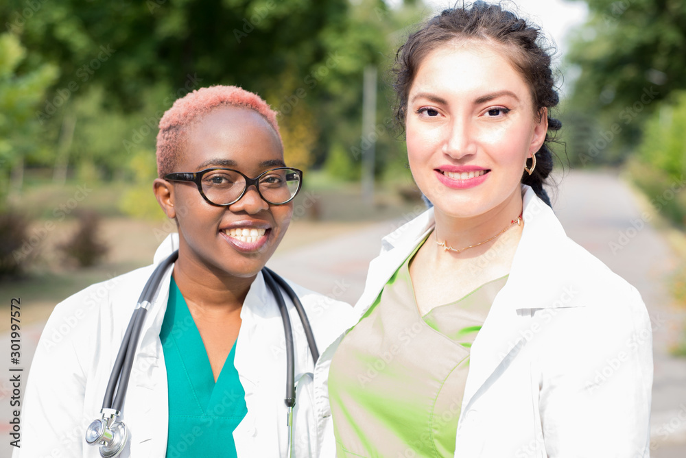 a pair of young doctors. Medical students laugh at white coats and with a stethoscope. Outdoor a pair of young doctors. Medical students laugh at white coats and with a stethoscope. Outdoor