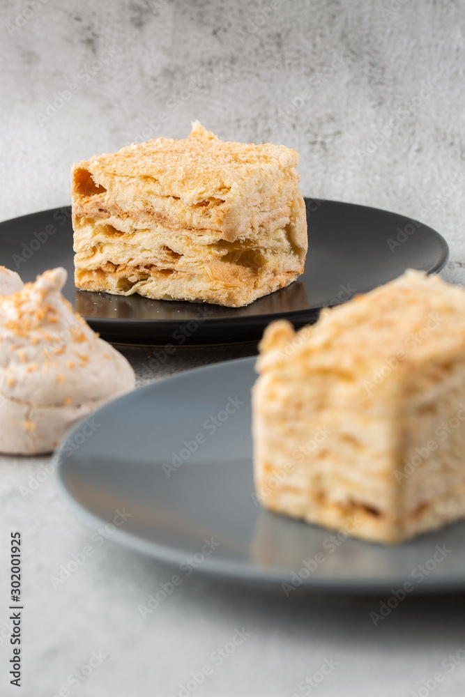 Piece of cake Napoleon on blue plate on marble background, close up view. Traditional millefeuille dessert with puff pastry and custard, copy space. Vertical photo. Photo for bakery menu. Piece of cake Napoleon on blue plate on marble background, close up view. Traditional millefeuille dessert with puff pastry and custard, copy space. Vertical photo. Photo for bakery menu.