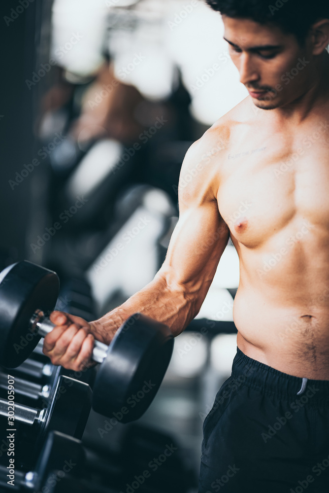 Muscular bodybuilder guy doing exercises with dumbbells in gym Muscular bodybuilder guy doing exercises with dumbbells in gym