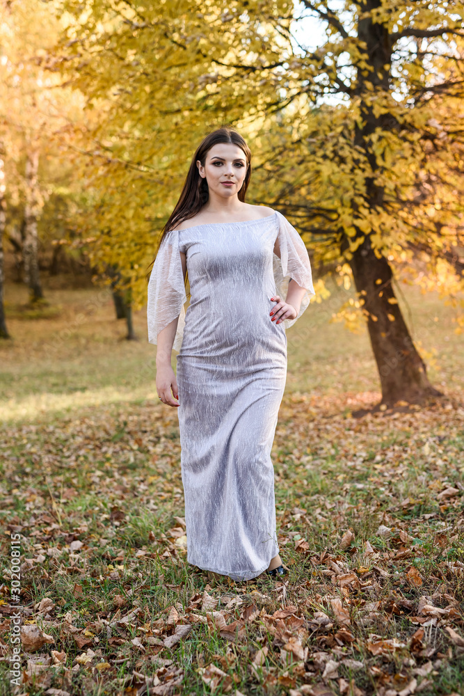 Woman in elegant evening dress posing in autumn park. Sunlights on trees in yellow colours