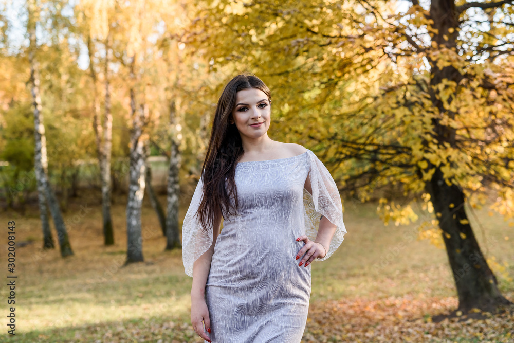 Woman in elegant evening dress posing in autumn park. Sunlights on trees in yellow colours Woman in elegant evening dress posing in autumn park. Sunlights on trees in yellow colours