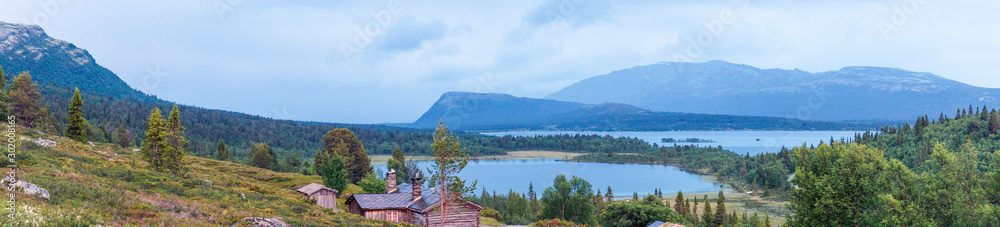 Panorama shot of Old farm houses and gravel road leading towards lakes and mountains in the background. Landscape and travel concept.