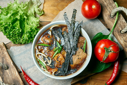 Vegetarian bowl with ramen soup, shiitake mushrooms, soy meat on a wooden tray in a composition with fresh vegetables. Healthy food.