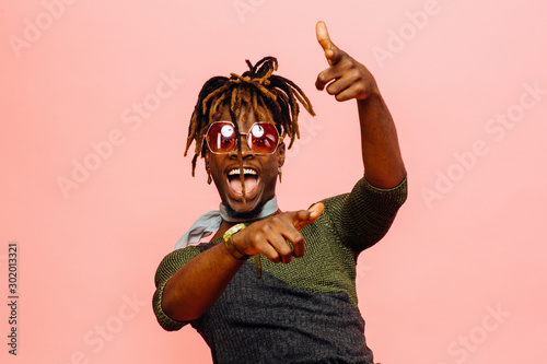 Portrait of a fun young man with mouth open laughing and pointing at camera, isolated on pink