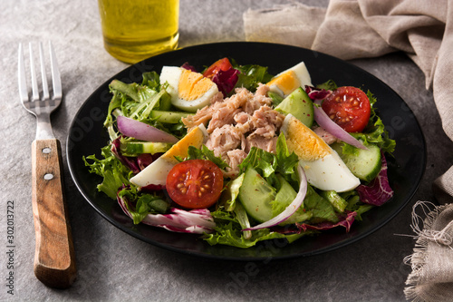 Salad with tuna, egg and vegetables on black plate and gray background 