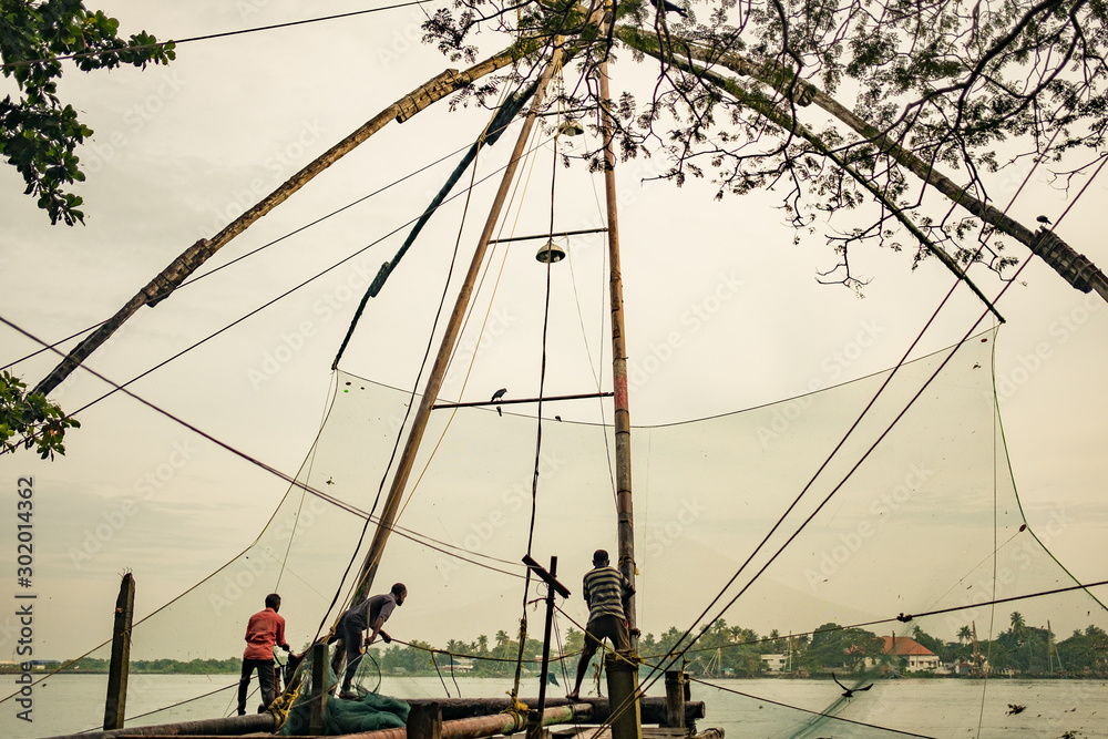 Cochin, India - 20 august 2019: fishermen stand on traditional chinese fishing nets structure  in early morning with warm natural soft light