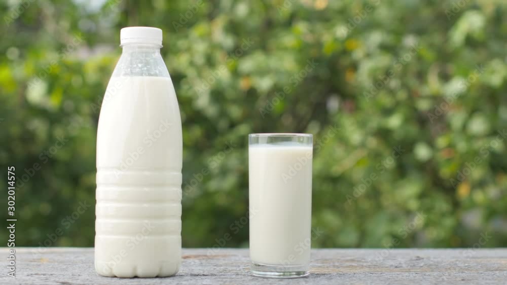 Male hand puts a glass of fresh milk on a wooden table, next to it is a bottle of milk. Organic products. Natural green background. Healthy food concept. Male hand puts a glass of fresh milk on a wooden table, next to it is a bottle of milk. Organic products. Natural green background. Healthy food concept.