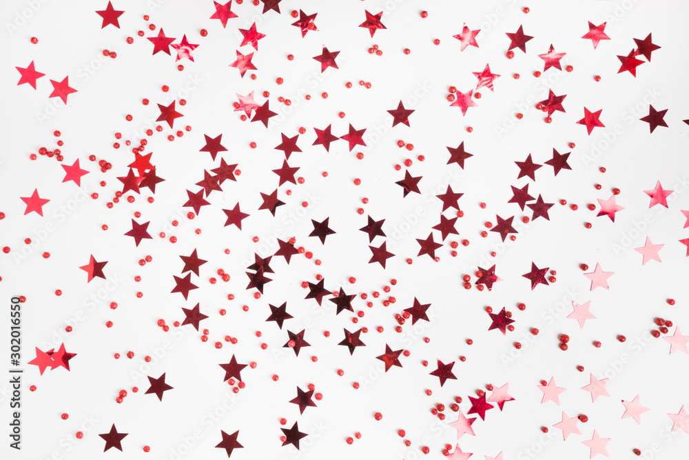Party holiday backdrop with red stars glitter confetti on white background. View from above, flat lay style. Xmas template. Happy New Year.