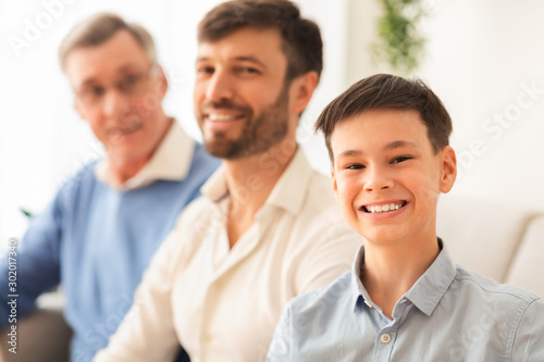 Boy With Father And Grandfather Sitting On Couch At Home