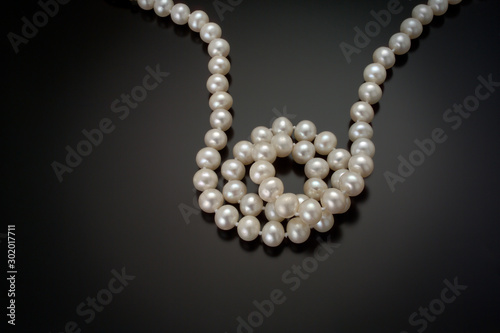 A strand of white round cultured pearls curl in the center of a black reflective background.