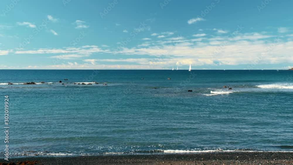 Unrecognized white sailboats in the turquoise waters of the ocean. Black volcanic sand beach. Freedom concept. Unrecognized white sailboats in the turquoise waters of the ocean. Black volcanic sand beach. Freedom concept.