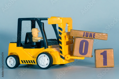 june 1st. Day 1 of month,  Construction or warehouse calendar. Yellow toy forklift load wood cubes with date. Work planning and time management. summer month, day of the year concept