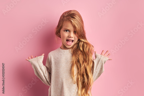 Portrait of surprised caucasian girl with sweet appearance look at camera, have long hair with long waves, wearing white blouse, isolated pink background