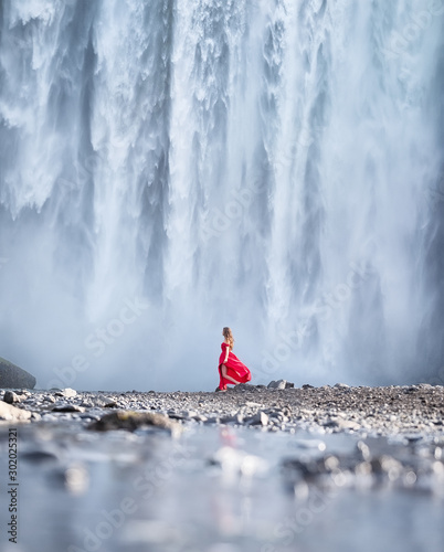 Girl in red dress on the Skogafoss waterfall background. Travelling on Iceland. Tourist in the famouns place in Iceland. Travel - image photo