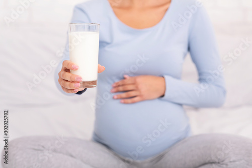 Unrecognizable Pregnant Woman Offering Glass Of Milk Sitting On Bed