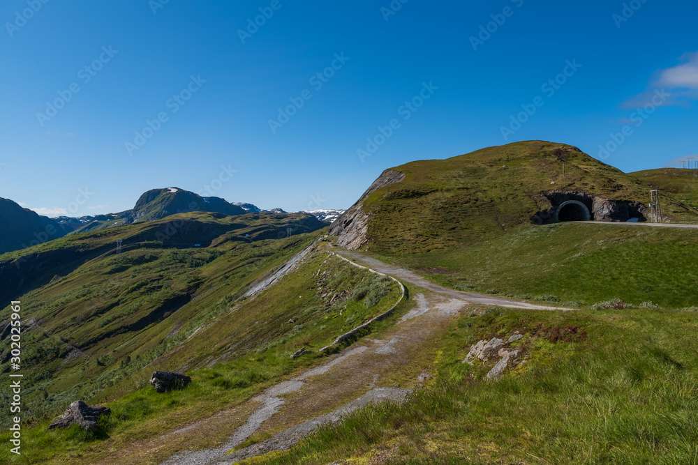 Fototapeta premium Through the Vikafjell a pass road to Vik is located in the kommunes Hordaland and Sogne og Fjordane. Mountains with summer snow on background. July 2019