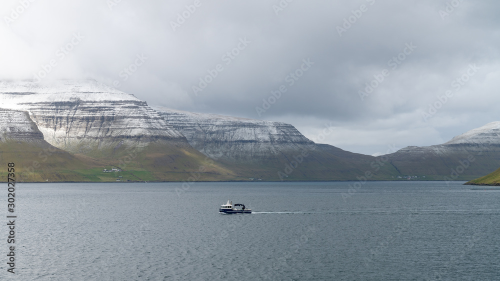 Fishing boat sailing through dramatic landscape on Faroe Islands
