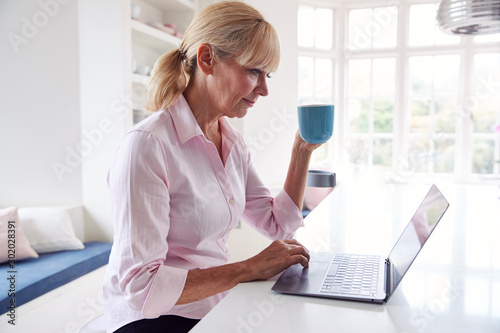 Mature Disabled Woman With Crutches At Home Working On Laptop On Kitchen Counter