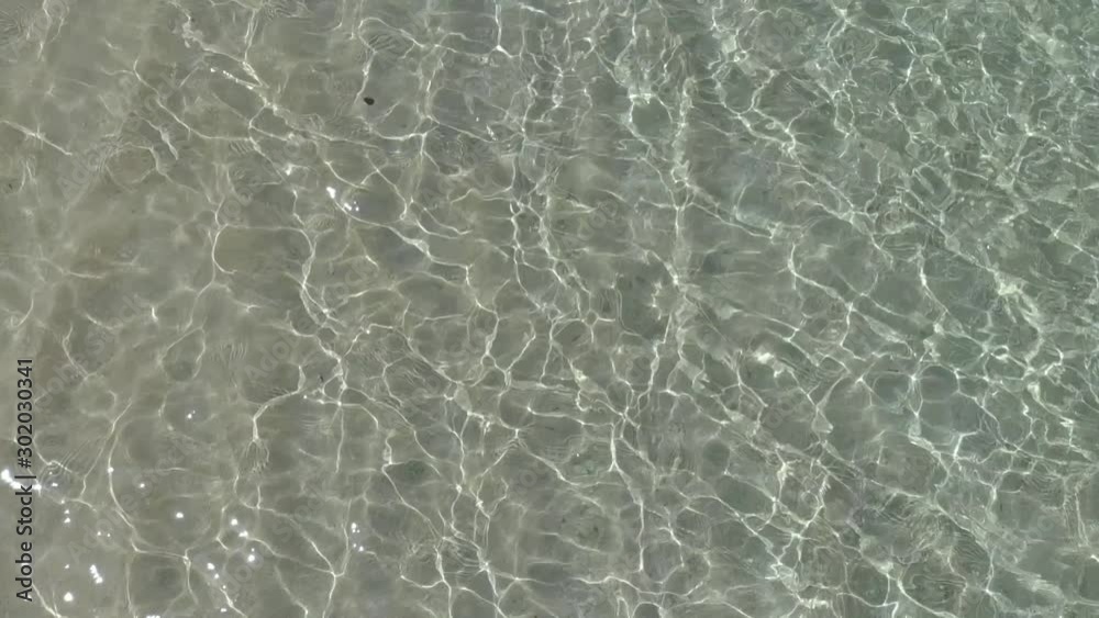 Zooming in view of crystal clear turquoise water on a shallow beach reflecting the midday sun. Zooming in view of crystal clear turquoise water on a shallow beach reflecting the midday sun.