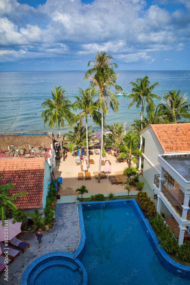 Phu Quoc island, Vietnam - March 31, 2019: hotel with pool on the coastline of the Indian Ocean, high palm trees, boat on the water.