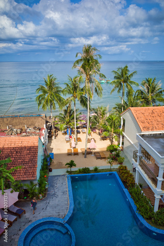 Obraz na płótnie Phu Quoc island, Vietnam - March 31, 2019: hotel with pool on the coastline of the Indian Ocean, high palm trees, boat on the water. w salonie