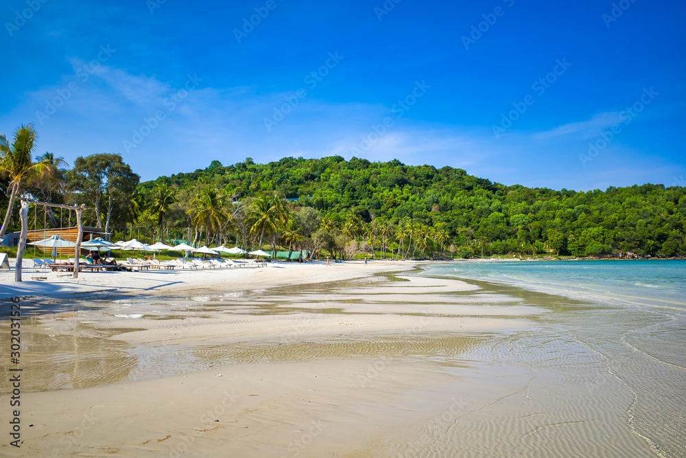 Sandy beach on the bay, high palm trees, blue sky, swings on the beach, sun loungers for relaxation and sunbathing under umbrellas, tourists resting, Phu Quoc island, Vietnam