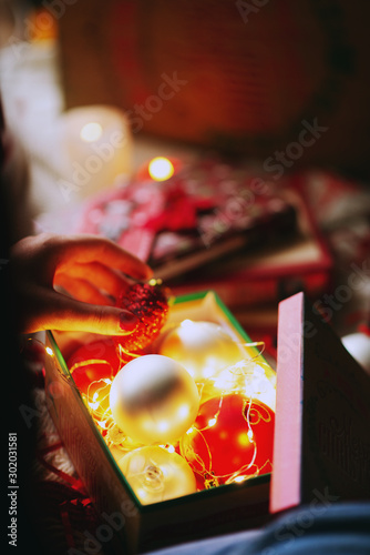 Celebrating New Year and Christmas at home, a girl wraps gifts and holds decorations for christmas tree in a cozy atmosphere