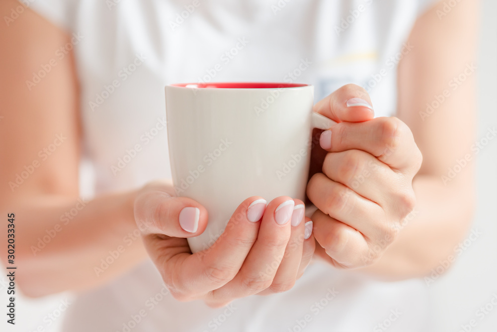Woman in a white t-shirt holds morning coffee in a white ceramic cup. Christmas concept. Front view Woman in a white t-shirt holds morning coffee in a white ceramic cup. Christmas concept. Front view