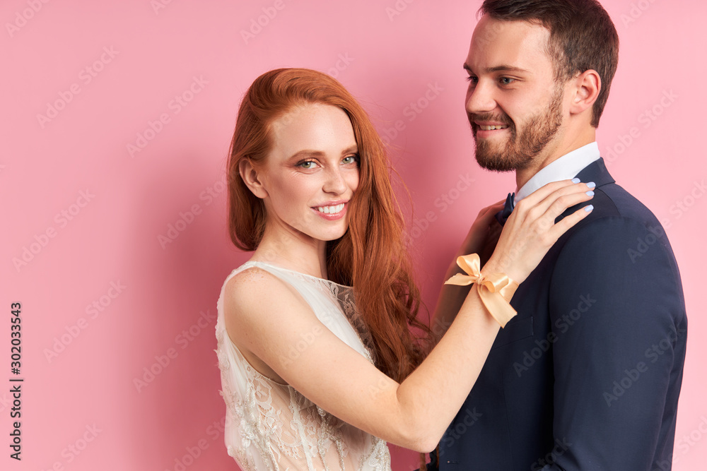 Caucasian couple of young two person stand hugging, posing at camera. Woman has red hair, man has beard Caucasian couple of young two person stand hugging, posing at camera. Woman has red hair, man has beard