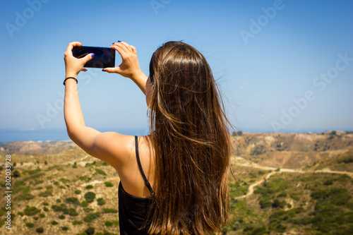 Summer trip to the sea coast. Young beautiful european girl travels, takes a photo on smartphone