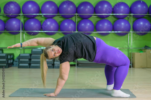 Fat woman is engaged in pilates in a fitness gym. A girl with a lot of overweight trying to lose weight with the help of sports and yoga, does the bridge exercise.