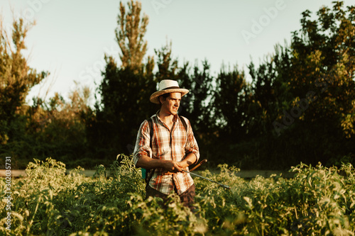 Young farmer spraying organic fertilizer with manual pump tank