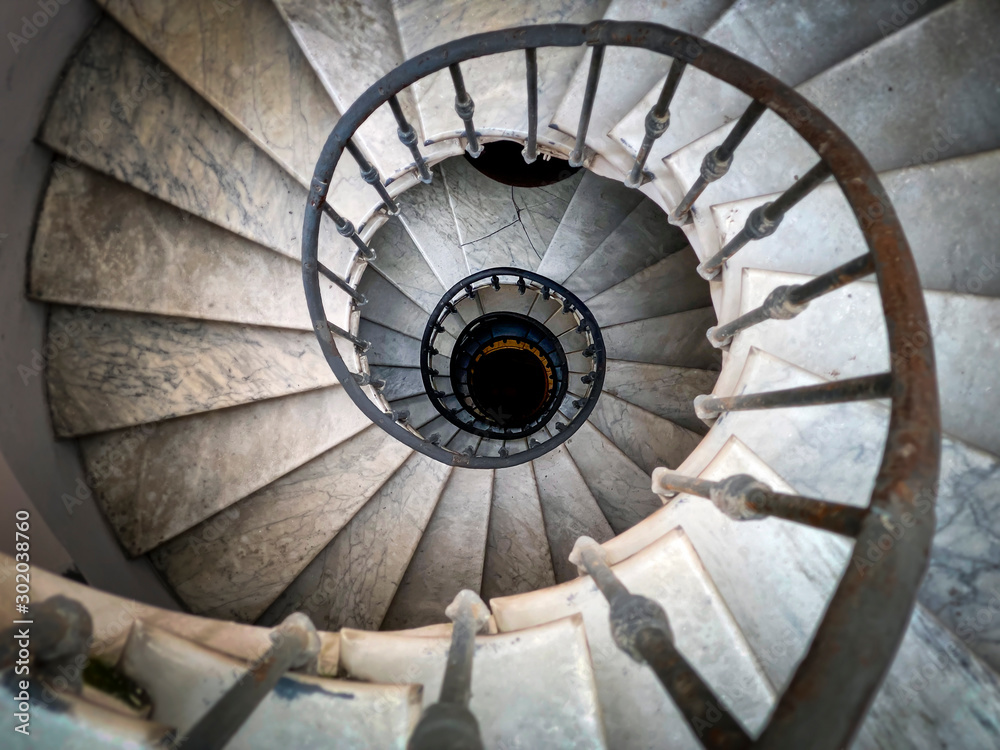 Ancient spiral staircase with decorated wrought iron handrails and marble steps inside an old palace in Rome.