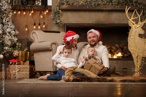 Image of parents with son at fireplace, deer with garland in room © Sergey