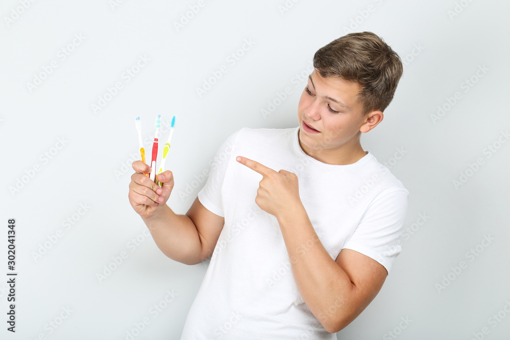 Young man with toothbrushes on grey background Young man with toothbrushes on grey background