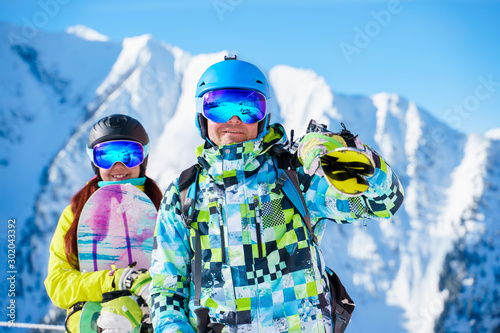Happy man and woman snowboarders standing on snow resort against backdrop of mountain.