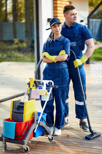 Portrait of young caucasian staff from cleaning service stand with detergents, cleaning equipment. look side