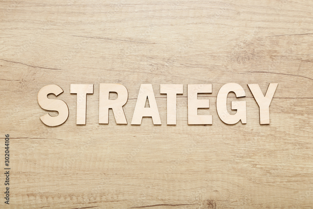 Naklejka premium Word Strategy by wooden letters on brown table