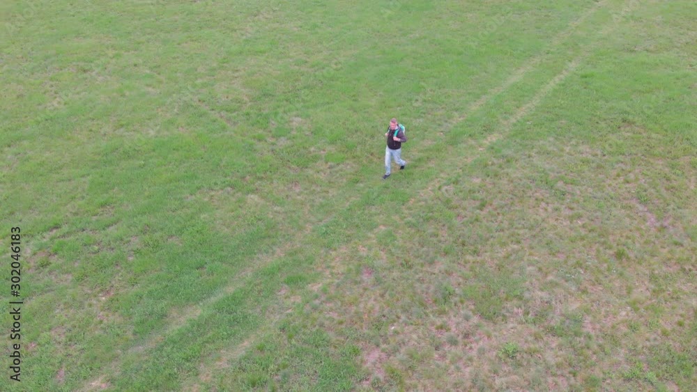 Handsome adult man hiker hiking in green grass meadow nature at springtime. Footage is recorded with camera attached to a flying drone. Handsome adult man hiker hiking in green grass meadow nature at springtime. Footage is recorded with camera attached to a flying drone.