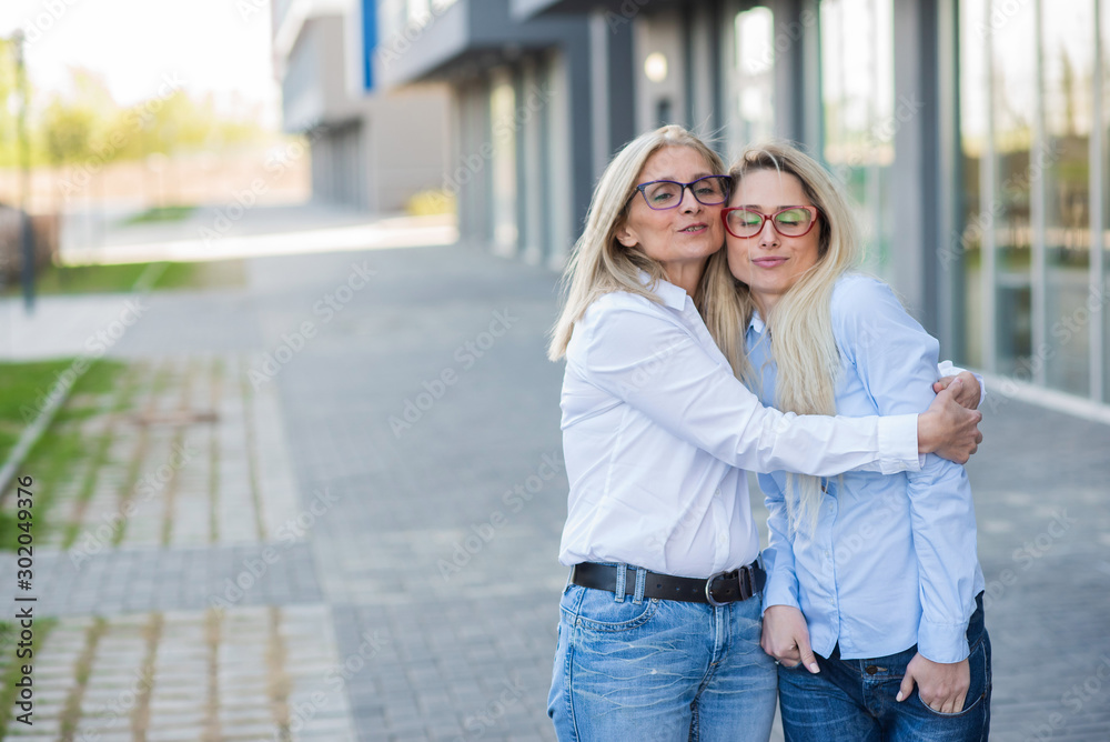 A beautiful blonde with glasses and her elderly mother are walking together. Mothers Day. Beautiful aged woman is a senior citizen and her adult daughter. Happy women of different generations.