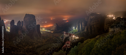 Meteora mountains and monasteries lit at night over Kastraki city glowing in distant fog