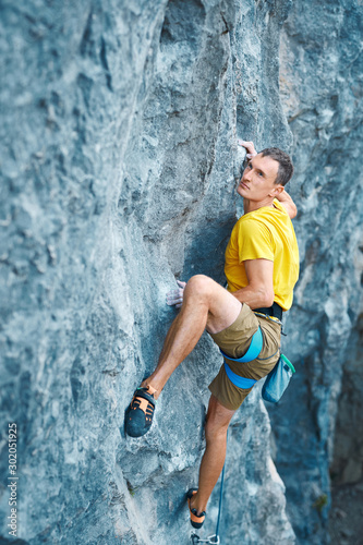 young strong man rock climber in yellow t-shirt, climbing on a cliff